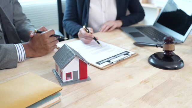 Lawyers reviewing a contract with a house model and gavel on the desk, representing real estate legal consultation, property agreement, and home ownership documentation.