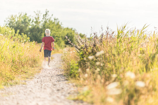Small child walking on narrow nature trail surrounded by tall grass.