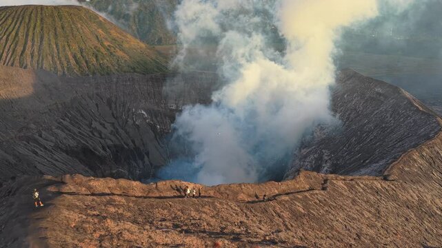 Incredible aerial view of tourists hiking on the rim of the active bromo volcano crater, with smoke billowing out from its center in java