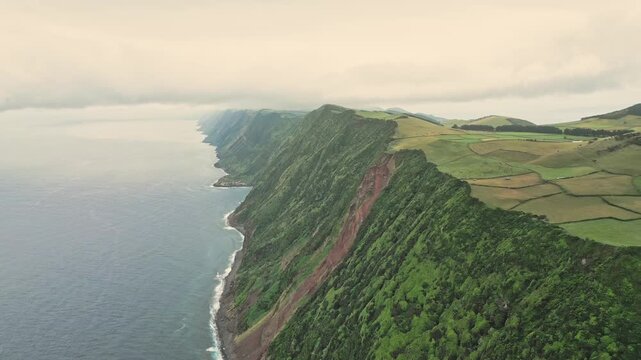 Aerial view along the Rosais sea cliffs on S&atilde;o Jorge Island, Azores, Portugal, with patchwork farmland above the Atlantic Ocean and under soft overcast misty skies