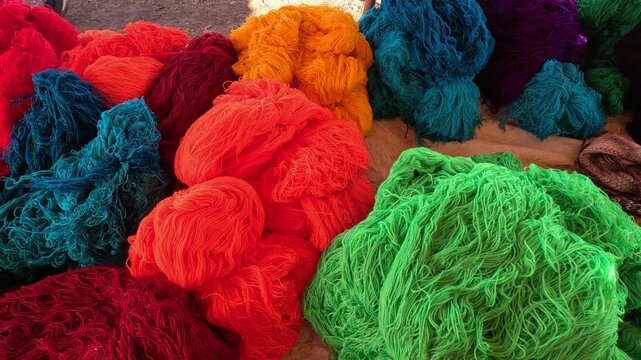 Bundles of brightly colored yarn stacked in an open-air market. Neon yellow, red, orange, teal, and green skeins ready for weaving, knitting, carpet making, or textile production.