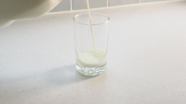 Milk poured steadily into a glass on a kitchen work surface