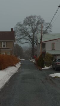 view of a quiet suburban street covered in fresh white snow. Rows of houses and leafless trees are visible under a grey winter sky.