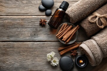 Aromatherapy setup featuring essential oil bottle, cinnamon sticks, black stones, white flowers, and rolled towels on rustic wooden surface