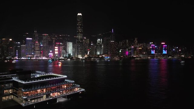 Panoramic aerial view of the illuminated skyscrapers and Victoria Harbour in downtown Hong Kong at night, showcasing the vibrant city lights and skyline.