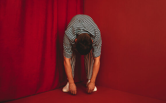 Person in striped clothing bending in red corner showing despair and burnout