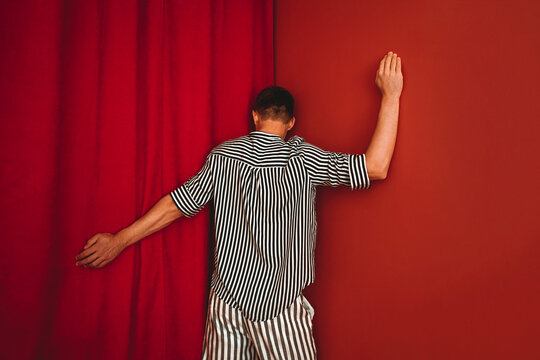 Person in striped shirt leaning against red wall in despair