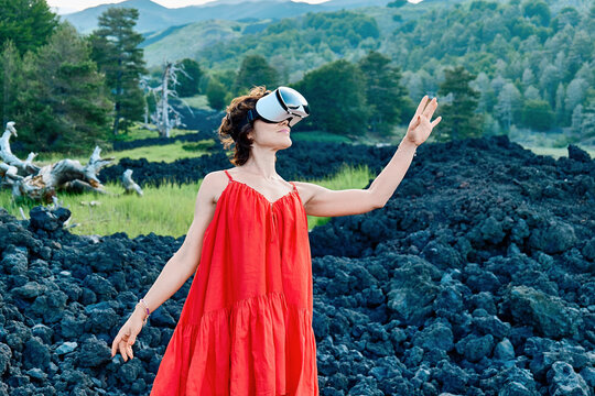 Woman in red dress using VR headset standing on volcanic Mount Etna