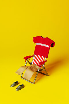Empty beach chair with summer outfit and shoes on bright yellow background
