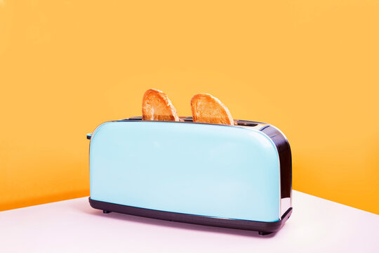 Blue toaster with golden bread slices on pink surface and yellow background