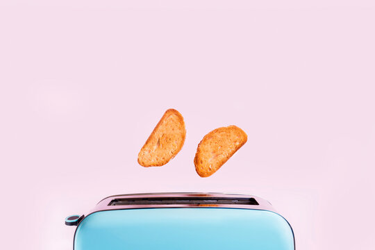Toasted bread flying from blue retro toaster on pink background