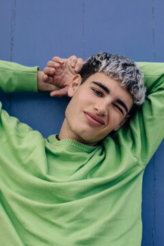Playful portrait of young man winking with hands behind head outdoors