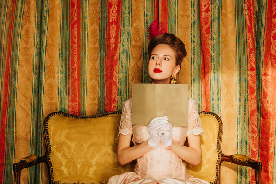 Woman in Rococo vintage dress reading a book on a vintage sofa