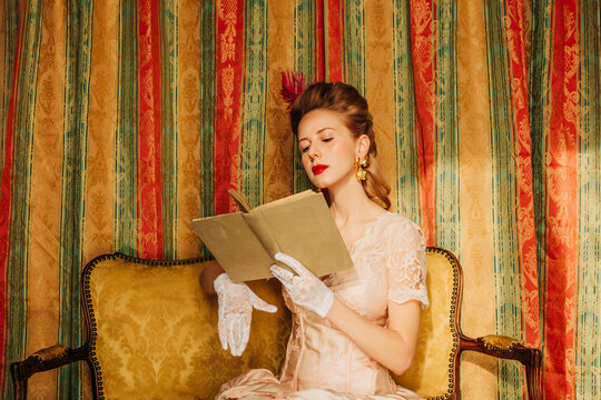 Elegant woman in rococo vintage dress reading a book indoors