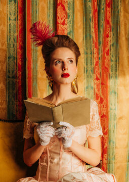 Elegant woman in rococo vintage dress reading a book indoors