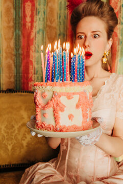 Surprised woman in vintage Rococo dress holding birthday cake with candles