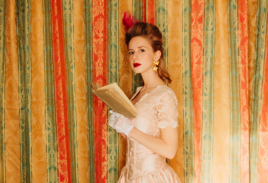 Vintage Rococo style woman reading book by ornate curtain indoors