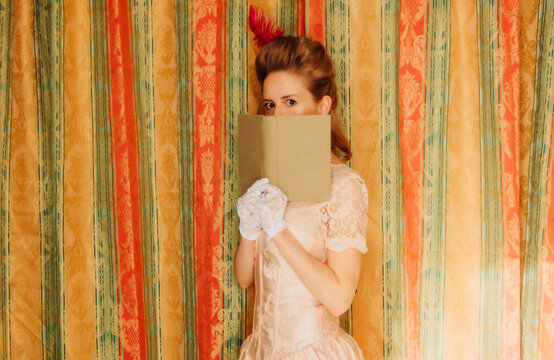 Woman in vintage Rococo dress reading a book and hiding face indoors