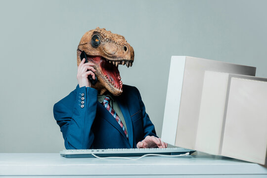 Person in dinosaur mask working at office with old computer and cell phone