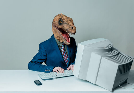 Person in business suit with dinosaur head working on old computer