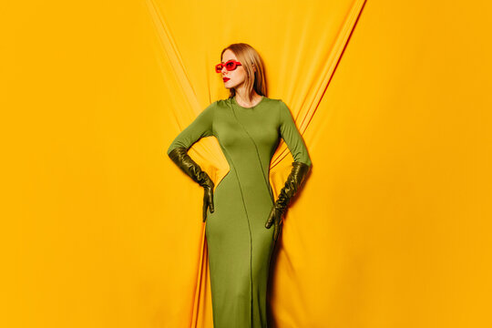 Stylish woman in green dress and red sunglasses against yellow background