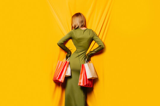Fashionable woman in green dress holding shopping bags on yellow background