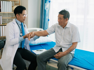 Obraz premium An Asian male doctor and an elderly patient join hands to perform physical therapy to assist the patient in a hospital ward.