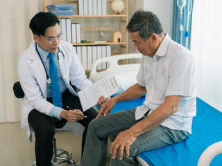 Obraz premium An Asian male doctor is examining an elderly male patient lying on a bed in a hospital ward, a healthcare concept.