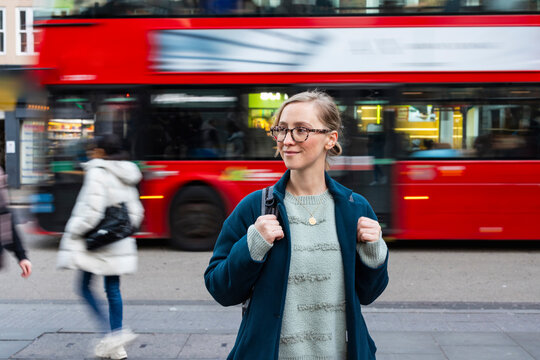 Woman standing on busy city street with red bus passing by