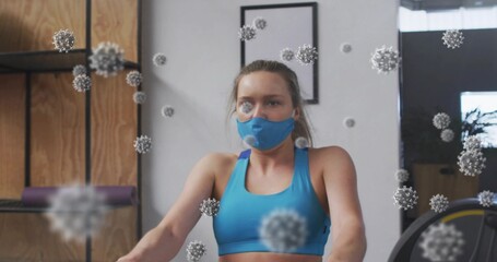Rowing woman wearing blue sports bra and mask in gym on rowing machine, virus particles floating