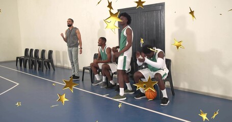 Clapping players and coach in green, standing, sitting on blue court, basketball and chairs seen