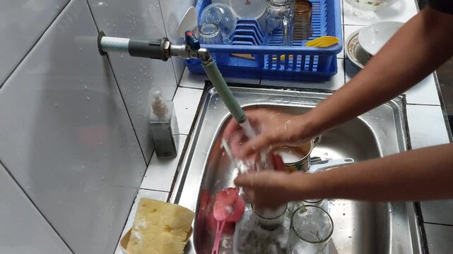 footage of a person washing dishes and glasses at a home kitchen sink. The video highlights everyday household chores, hygiene, and clean living.