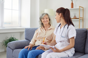 Obraz premium Senior woman in living room of nursing home talking to doctor, close-up. Nurse writing down symptoms of elderly patient. Concept checkup, health care, retirement home, healthcare and medicine