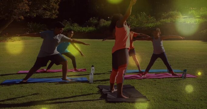 Instructor cueing students on mats, guiding mirroring yoga side-bend with lens-flare for fitness