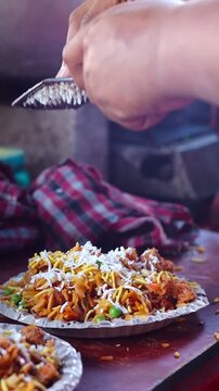 Vertical close-up video of a street vendor grating fresh cheese over a plate of delicious and spicy Indian street food chaa