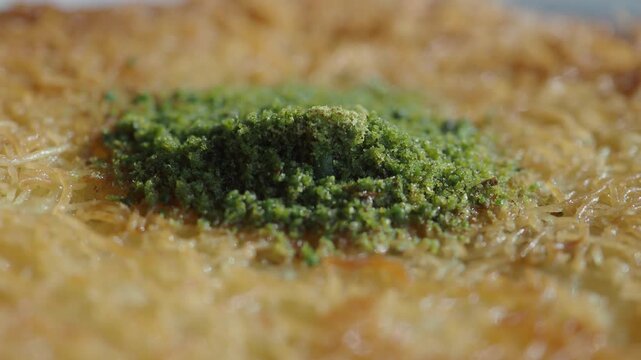 Close up of sweet kunafa pastry dessert with pistachios drizzled with syrup