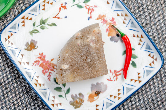 Closeup photograph of a single portion of homemade holodets, a traditional Russian cold meat appetizer (aspic or studen), on a square plate in a green bowl.