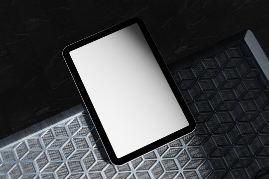 A sleek tablet with a blank white screen rests on a textured, honeycomb-patterned surface, set against a dark background