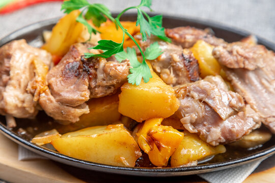 Sizzling cast iron skillet with braised kid meat and roasted potatoes on a wooden board, closeup.