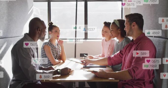 Man at right passing tablet in marketing meeting, team leaning as social icons and counts appearing