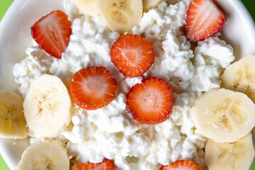Macro shot of fresh cottage cheese topped with juicy strawberry slices and banana. High-protein healthy breakfast bowl for nutritious diet and fitness lifestyle.
