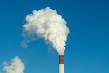 CO2, greenhouse gases emissions. CHP emissions. Smoking chimney releasing smoke against a blue sky....