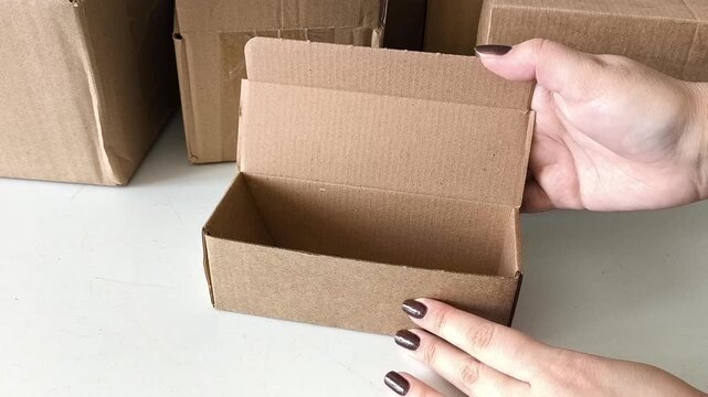 Female hands open a cardboard box on the table, there are many boxes in the background. Parcel warehouse. Delivery of goods by mail. Online store