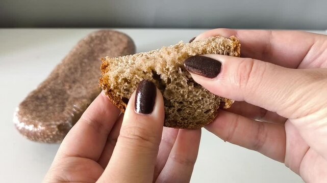 Women's hands break a piece of fresh whole-grain yeast-free bread, a package of dark flour bread on the table. Sourdough pastries
