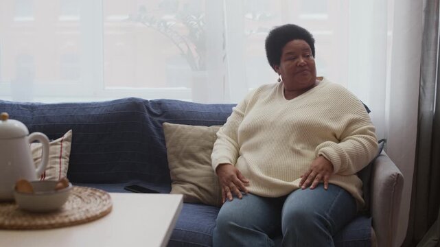 Medium shot of African American grandmother resting on sofa and checking grandsons grades