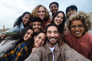 Obraz premium Big group portrait of diverse young people together outdoors. Multiracial happy millennial male and female friends having fun together. Unity and friendship concept. Focus on man in the center