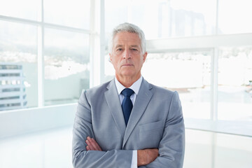 Senior man standing arms crossed wearing suit, tie by floor-to-ceiling office windows glossy floor © wavebreak3