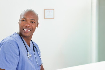 Adult African American man sitting at clinic reception desk with stethoscope in blue scrubs smiling © wavebreak3