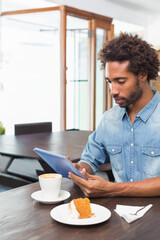 African American man sitting at table using blue tablet, coffee and cake in cafe, copy space