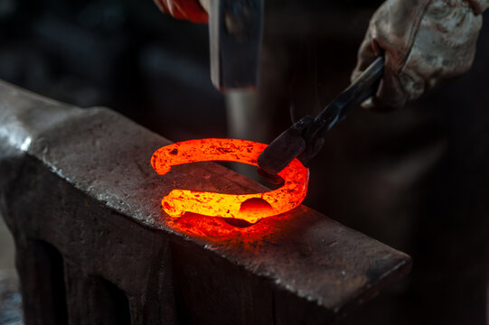 Blacksmith Forging a Glowing Horseshoe on Anvil. Close-up of a blacksmith forging a glowing hot horseshoe on an anvil. Traditional craftsmanship, strength, precision in a rustic workshop setting.	